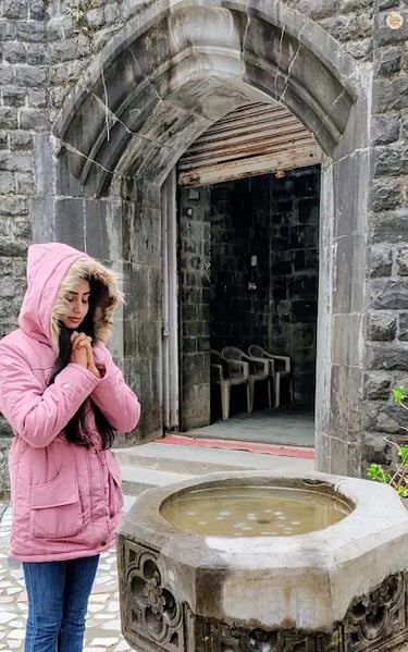 Visitor tossing a coin into the wishing well at St. John in the Wilderness Church, McLeod Ganj.