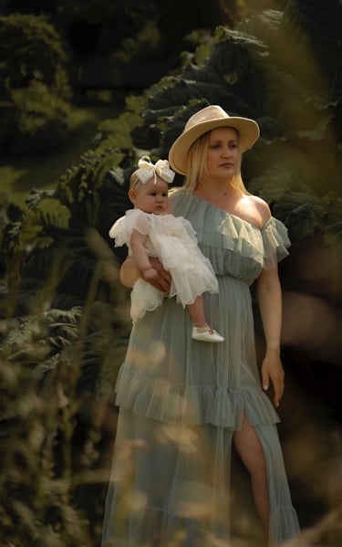 Mother in long dress and hat holding her daughter in the park 