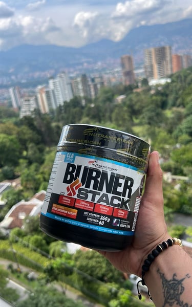 A hand holding a Nutramerican Pharma Burner Stack supplement container against a city skyline backdrop.