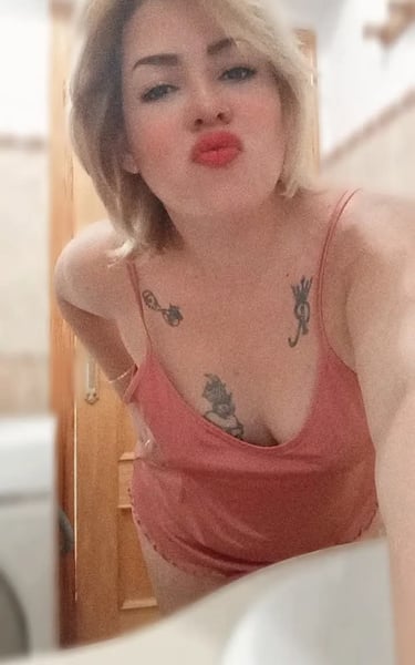 Selfie de Nikol con pijama rosa, labios sensuales y tatuajes visibles en el pecho