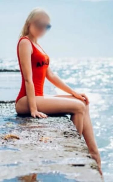 Ana sentada junto al mar en bañador rojo, mostrando su silueta perfecta y su piel dorada.