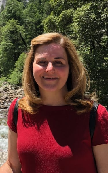 Kathy Fowler, owner and baker at Kitty's Confections, smiling outdoors in a red shirt