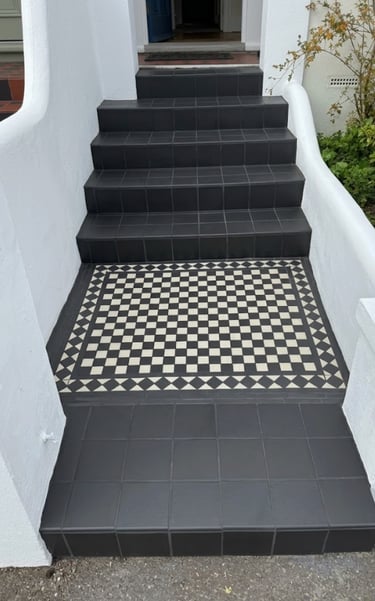 Bright front porch featuring black non-slip steps and a decorative checkerboard mosaic tile landing.