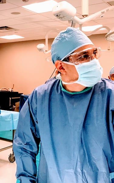 Surgeon in blue sterile scrubs, face mask, and eye protection in an operating room.