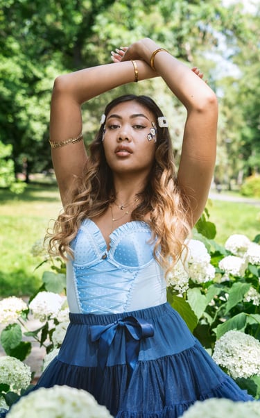Portrait photo of a young Indonesian woman in a park with flowers and whimsical blue dress