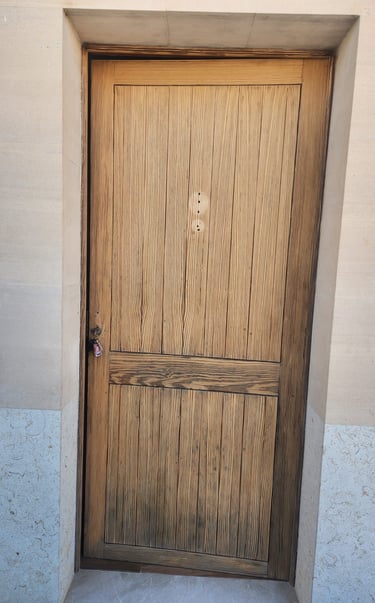 Rustic vertical grain wooden exterior door set in a stone door frame with a small key in the lock.