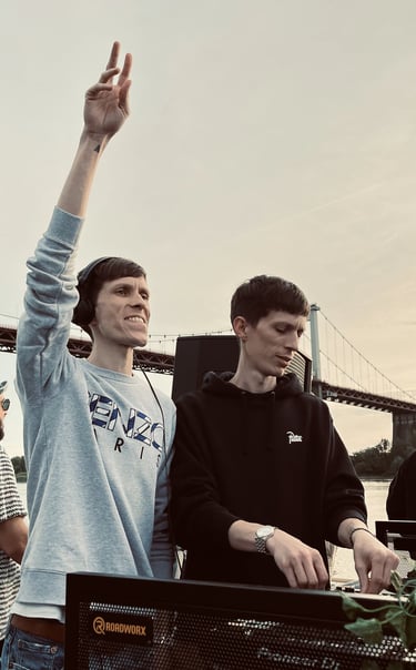 Two dj men standing in front of a large screen