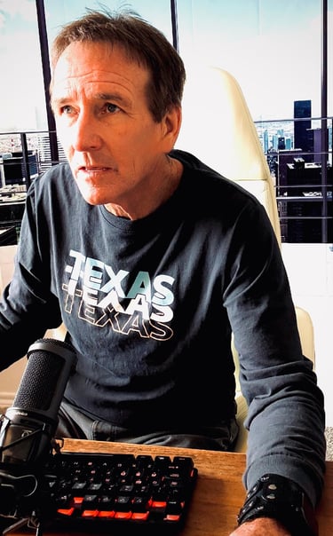 Podcaster wearing a Texas shirt sitting at a desk with a microphone and gaming keyboard.