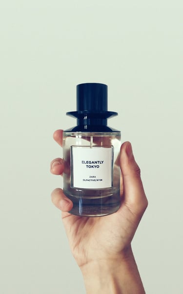 A hand holding a bottle of Zara Elegantly Tokyo Olfactive fragrance against a white background.