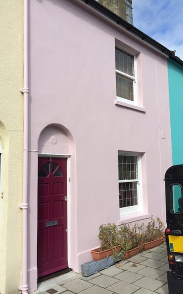 A Brighton pink terraced house with a burgundy door and white sash windows.