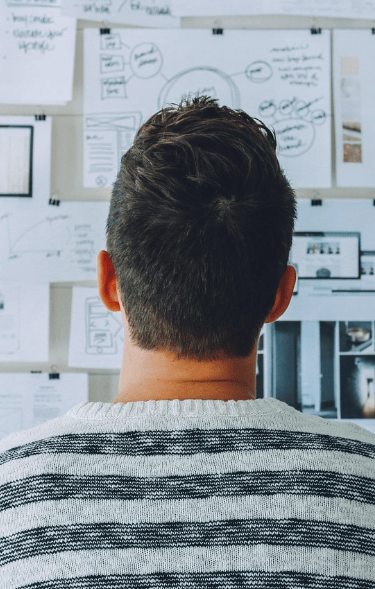 Persona espalda, suéter rayas, mirando tablero ideas.