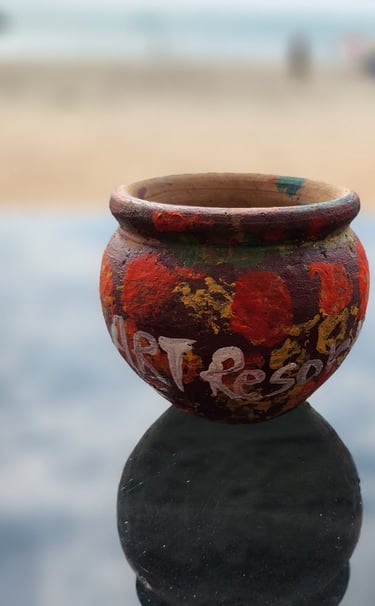 Hand-painted clay pot with colorful patterns reflecting on a glass table at a beach resort.