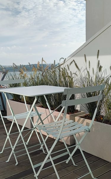 Stylish outdoor patio with light blue folding chairs and table, potted ornamental grass, and a distant river view under a