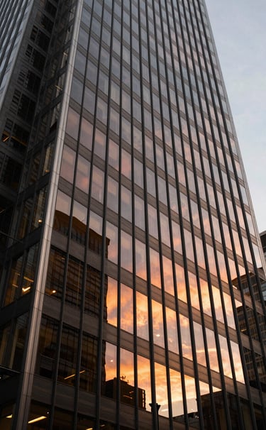 A low-angle cinematic shot of a modern Sydney skyscraper's glass facade reflecting the orange hues of a sunset, captured with a high-end photography style emphasizing clean lines and creative perspective.