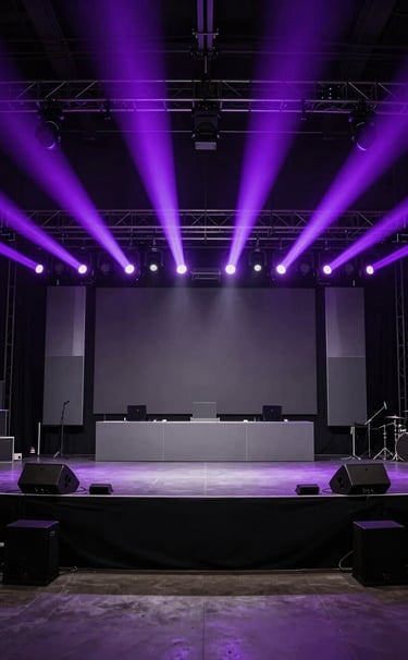 A wide shot of a high-end music event stage in a Spanish / Latin American venue. Professional lighting rig beaming vibrant electric violet rays through a misty atmosphere. Minimalist stage design with clean lines and steel grey accents. Solid, professional aesthetic in rich deep black tones.