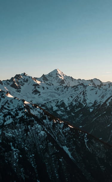 A wide-angle landscape photograph of a snow-capped mountain range in North America under a steel blue morning sky. The lighting is crisp and clear, emphasizing the rugged peaks and the serene atmosphere. The style is modern and minimalist, with a deep teal and muted green palette reflecting the pristine wilderness.