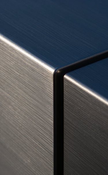 Macro photography of a brushed steel surface with sharp, geometric edges. The lighting creates dramatic shadows in deep blue and charcoal tones, emphasizing a clean and cutting-edge industrial design aesthetic found in high-end North American architecture.