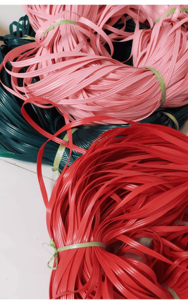 Colorful recycled plastic weaving strips in red, pink, and green prepared for handmade woven bag crafting at Craftvitas
