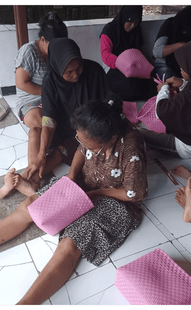 Artisan weaving a pink jali jali plastic woven bag by hand at Craftvitas Indonesia.