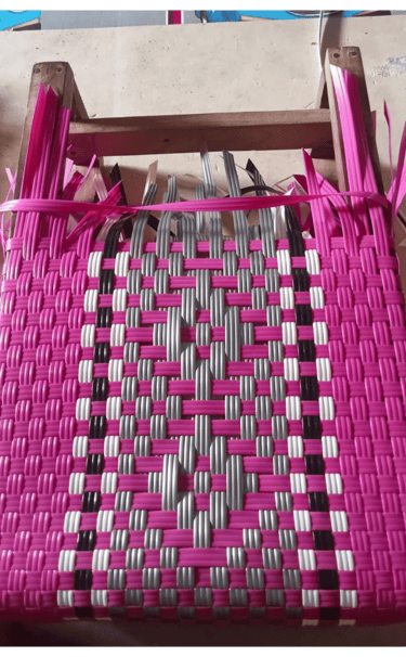 Early weaving process of a pink patterned handmade plastic woven bag at Craftvitas Indonesia.