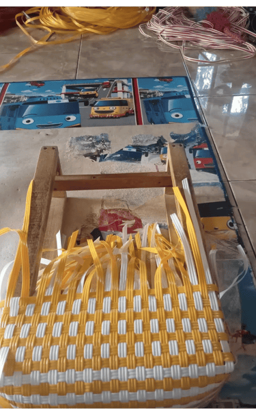 Shaping the base of a yellow and white handmade woven bag using recycled plastic weaving strips at Craftvitas Indonesia.