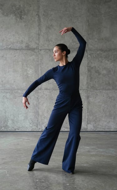 A full-length artistic photography shot of a performer in a minimalist concrete gallery space. The subject is posed in a vogue-inspired stance, wearing futuristic dark blue textiles. North American / US setting, professional fashion photography.