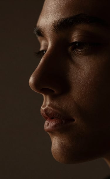 A minimalist close-up of a face partially obscured by deep shadows. The lighting is Warm Bronze, catching only the edge of a profile. Sophisticated, intimate, and dark aesthetic.