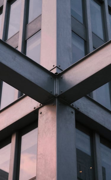 A macro photography shot focusing on the intersection of two steel beams on a modern US skyscraper. The color palette features charcoal gray and a hint of soft pink light reflecting off the metal. The composition is balanced and perfectly symmetrical, echoing Bauhaus design.