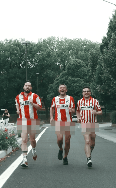 Three men jogging outdoors wearing red and white striped soccer jerseys for a charity run.