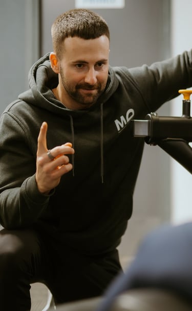 Personal trainer in hoodie coaching client on gym equipment in Leamington Spa fitness centre, focused on technique and su