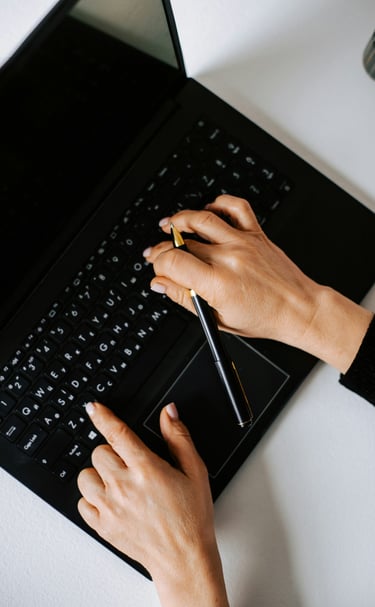 A person holding a pen and typint on a black laptop