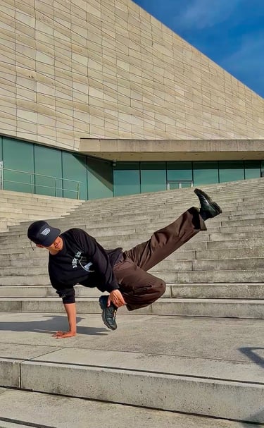 YoYo performing a breakdance move in front of concrete building.
