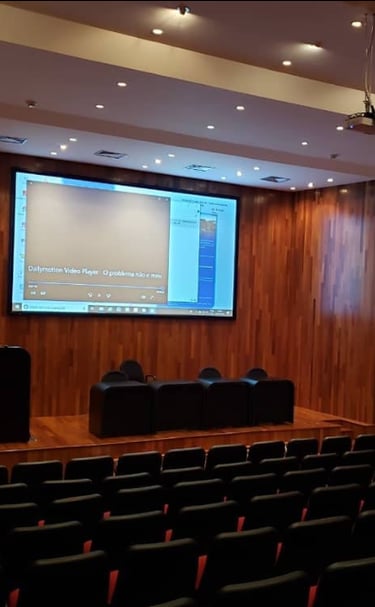 Tela elétrica e projetor em auditório grande com cadeiras pretas