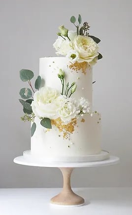 a white cake with white flowers and gold foil