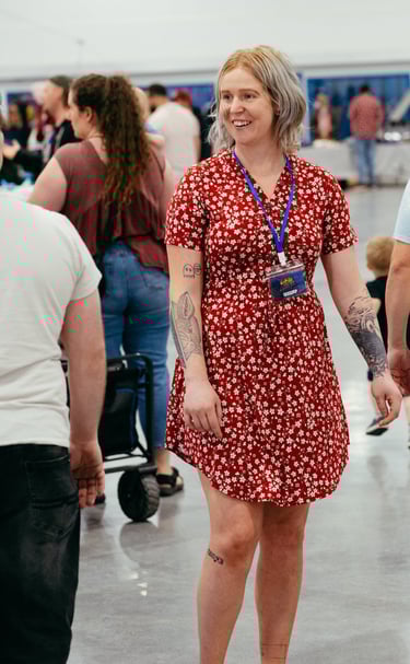 A woman in a red dress with a volunteer badge smiles at event goers