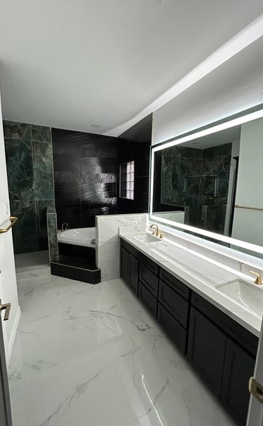 Modern master bathroom with white marble floors, a double vanity, and a black accent tile shower.