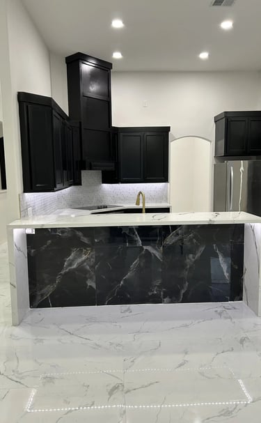 Modern luxury kitchen featuring a black marble island, white quartz countertops, and sleek black cabinets.