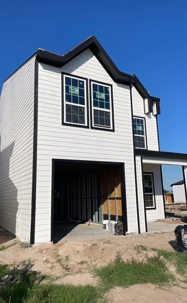 A modern two-story house under construction with white horizontal siding and black window frames.