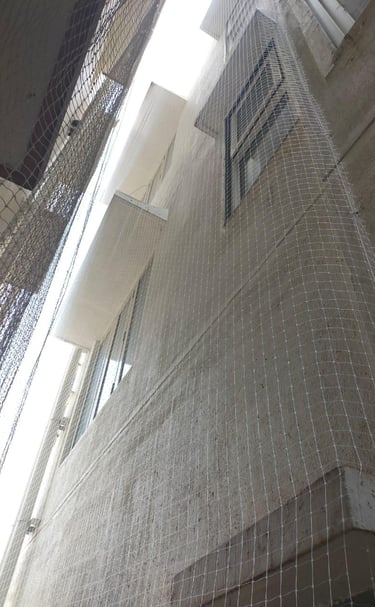Technician from Arjilli Enterprises installing a durable mesh net over an apartment duct area.