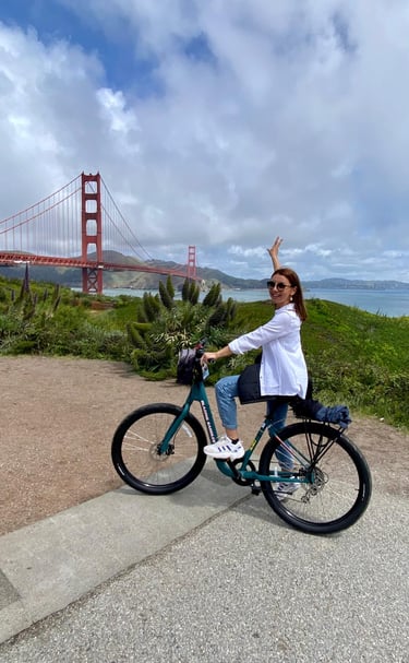 a woman riding a bicycle with a bridge in the background