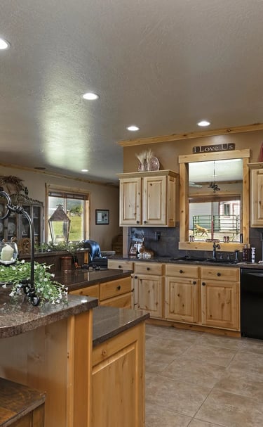 a kitchen with a large island and a black refrigerator, custom wood cabinets, and granite tops