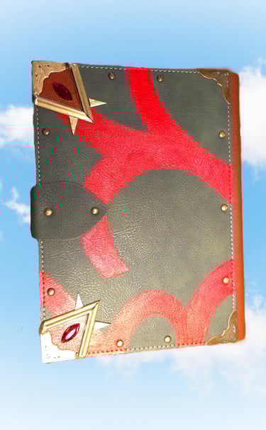 Handcrafted leather grimoire with red inlay, brass corners, and ruby gems floating against a blue sky.