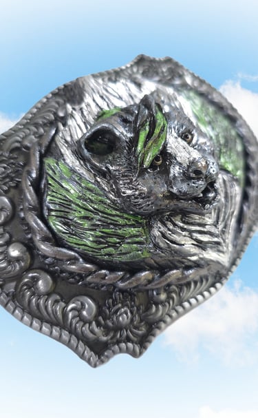 Vintage western silver bear belt buckle with green paint accents set against a blue sky background.