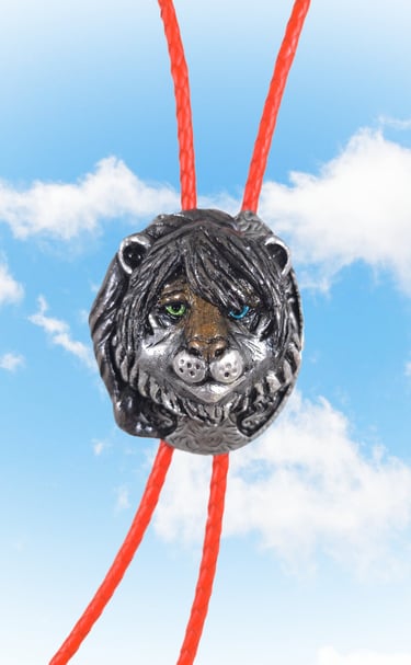 A silver lion head bolo tie with green and blue eyes on a red braided cord against a blue sky.