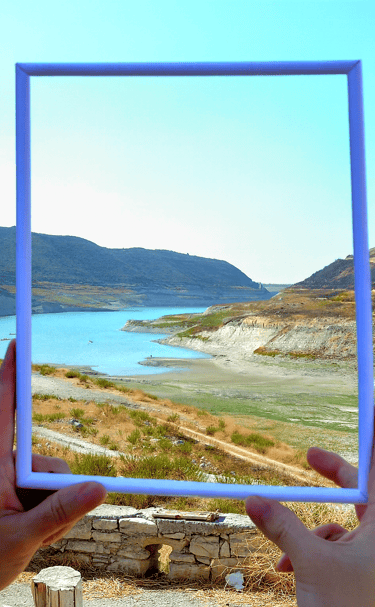 a person holding a picture frame with a picture of a lake