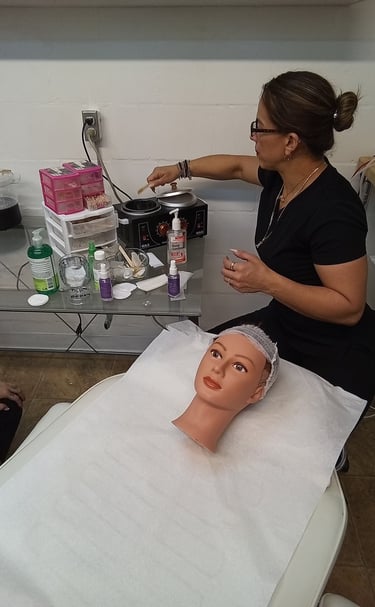 A beauty student practices facial waxing techniques on a mannequin head using a professional wax warmer.