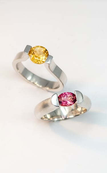 a pair of tension set sterling silver rings set with a pink tourmaline and the other a citrine.