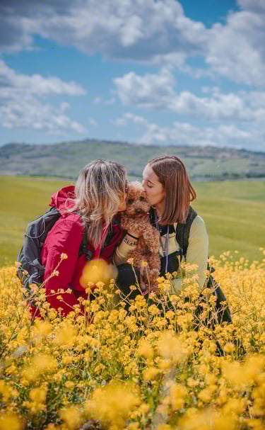 due donne danno un bacio a un cane in campagna tra fiori gialli