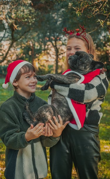 un bambino con un cappello natalizio e una bambina con un cerchietto natalizio abbracciano un cane