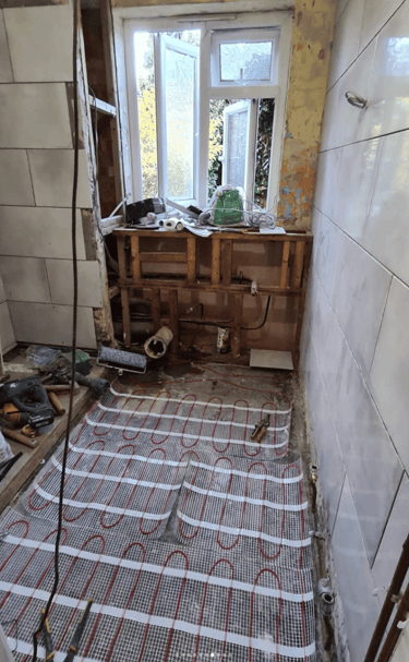 A bathroom under renovation with underfloor heating mats installed, partially tiled walls, and expos